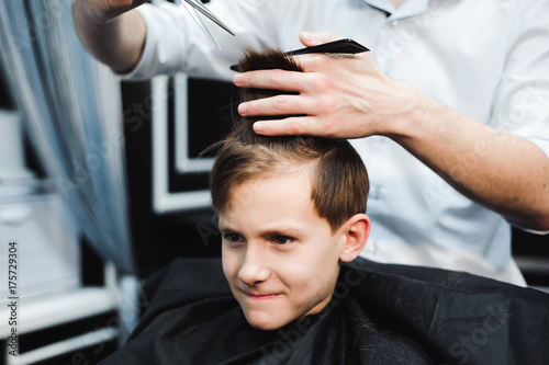 Cute little boy is getting haircut by hairdresser at the barbershop