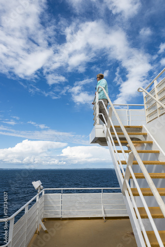 adult woman in blue sweater on ferry with blue sky and white clo