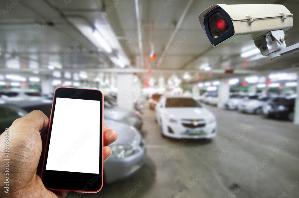 hand holding smart phone monitoring and CCTV security indoor camera system  operating with under ground indoor car parking garage area, internet,  surveillance security and safety technology concept Stock-Foto | Adobe Stock
