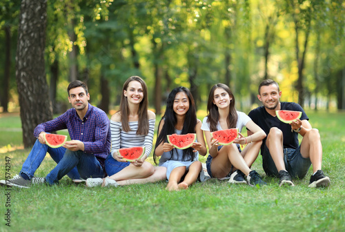 Portrait of friends sitting on grass with fresh watermelon