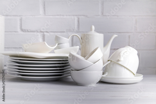 White porcelain  dishware stacked on a wooden table against white brick background. Concept of restaurant, cooking and service. © Studio Dagdagaz