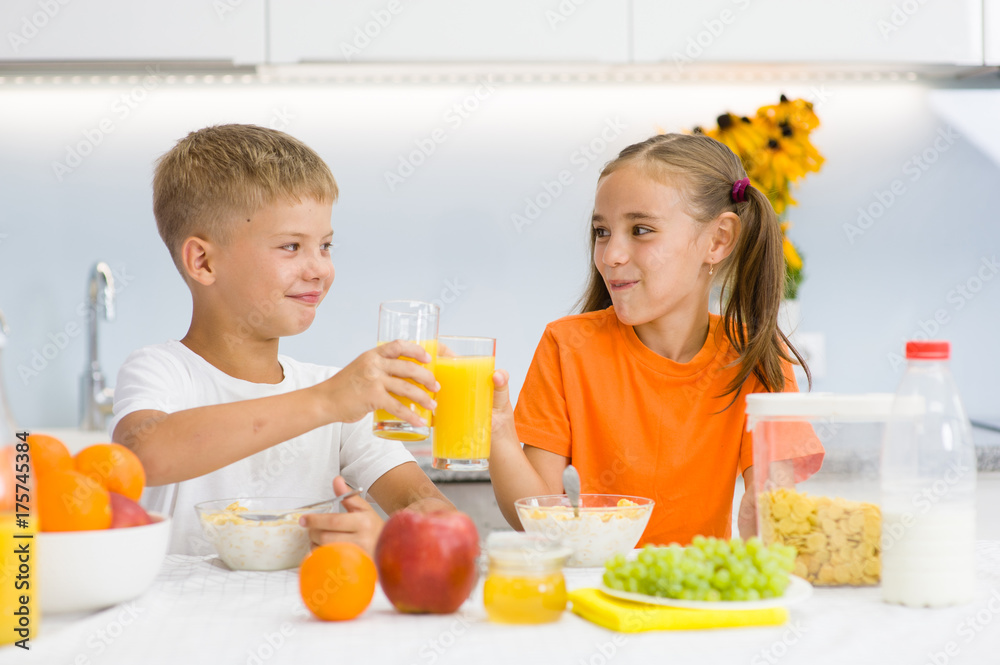 Brother with sister clink glasses with orange juice at breakfast Brother with sister clink glasses with orange juice at breakfast