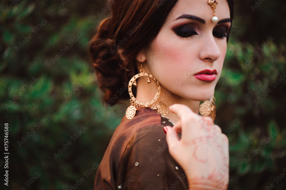 Beautiful young caucasian woman in traditional indian clothing sari with bridal makeup and jewelry and henna tattoo on hands
