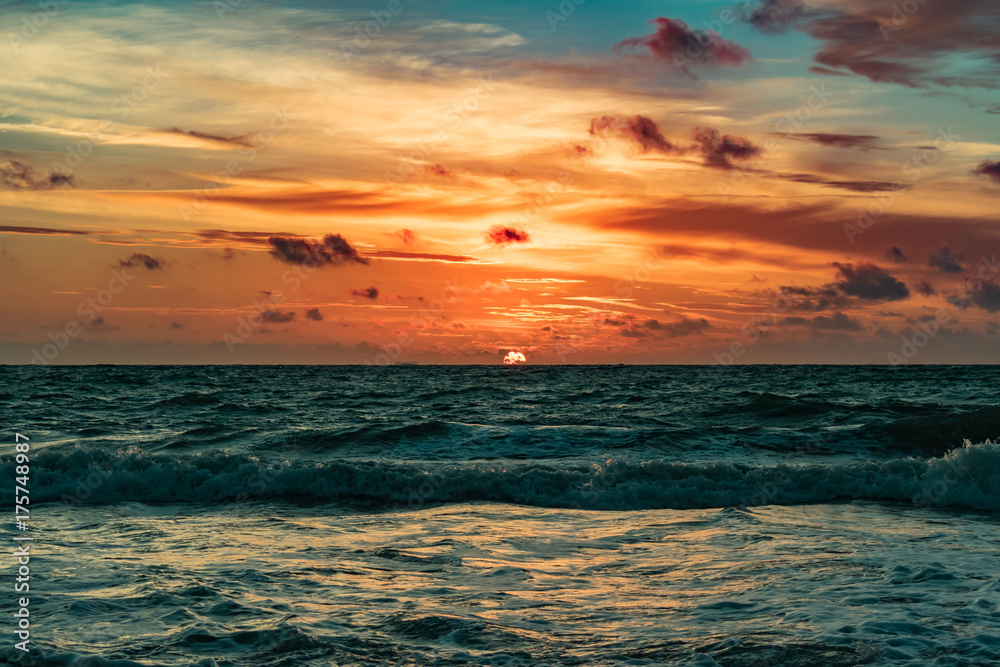 orange sun rising on the horizon on a windy morning with wavy green waters