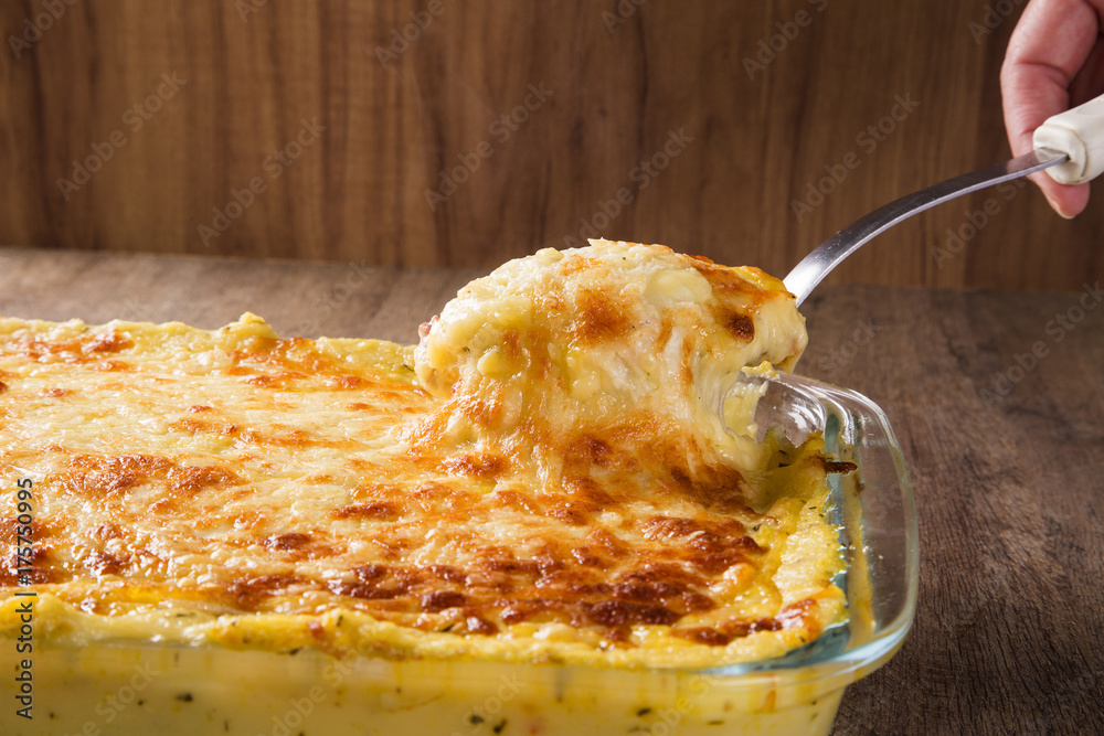 Hearty potato gratin with ham and parmesan cheese, cream and delicious cured bacon from South Tyrol freshly served from the oven on a wooden table