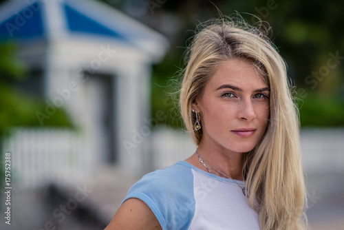 Summer Closeup portrait of beautiful blond girl with long hair and beautiful eyes poses against a white fence . She smiles at the camera