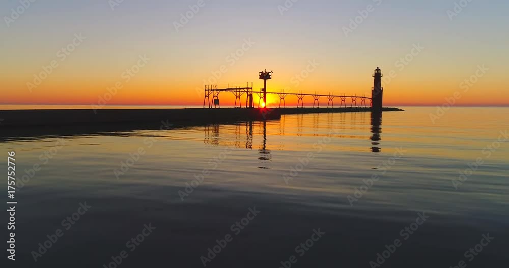 Fishermen, pier, and Lighthouse silhouetted against fiery Lake Michigan Sunrise over tranquil waters, moving low aerial view. Fishermen, pier, and Lighthouse silhouetted against fiery Lake Michigan Sunrise over tranquil waters, moving low aerial view.