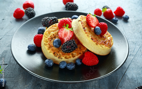 British Crumpets breakfast with blueberries, strawberries, blackberries, raspberries drizzled with icing sugar photo