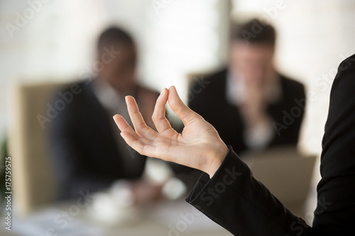 Close up image of female palm with fingers folded in Jnana mudra gesture with blurred silhouettes of talking businessmen on background. Businesswoman feeling calm, keeping mind in peace and clarity