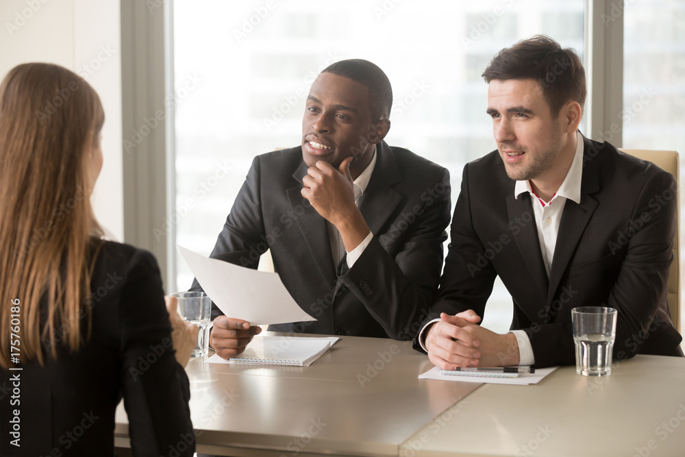 Φωτογραφία Afro american company leader with caucasian hiring manager listening and reviewing female job applicant after reading resume or CV