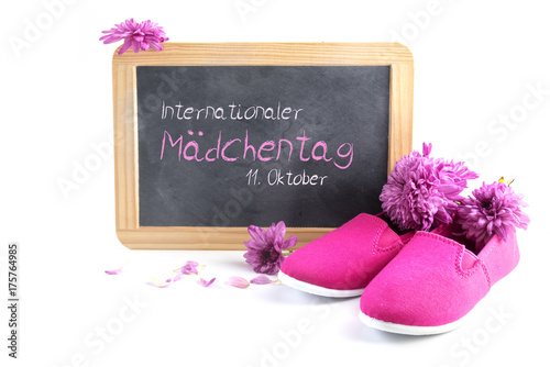 pink kid shoes and flowers against a writing blackboard with german text Internationaler Maedchentag, that means International Day of the Girl Child, isolated on white, date11 October photo