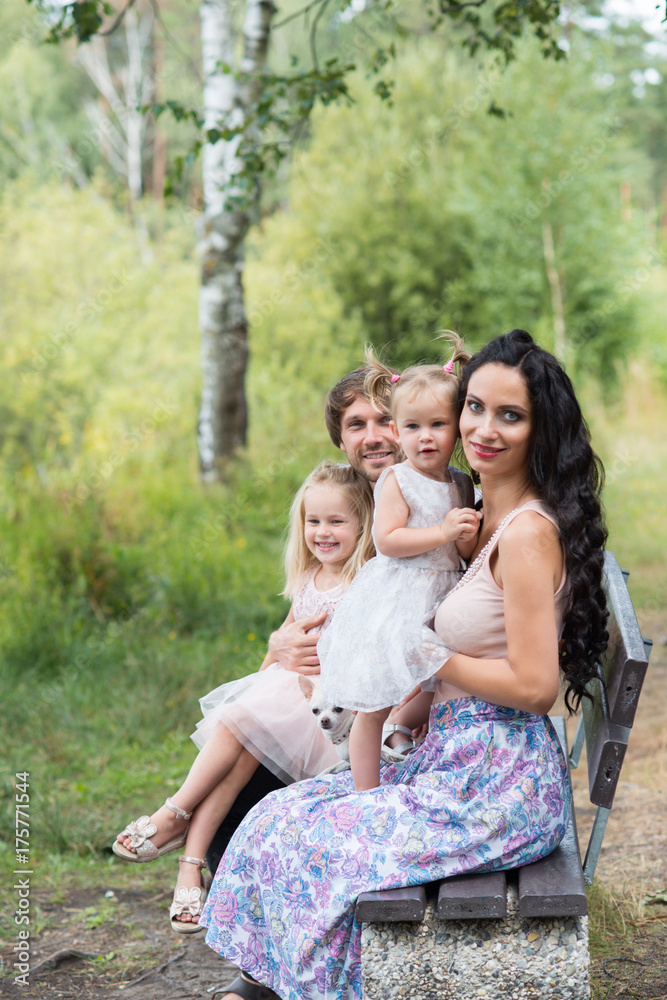 Beautiful young family with two daughters walking in the forest in summer Beautiful young family with two daughters walking in the forest in summer