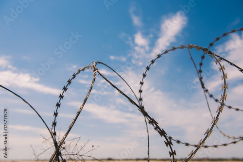 wire and blue sky with clouds. Safety fence of barbed wire against the blue sky