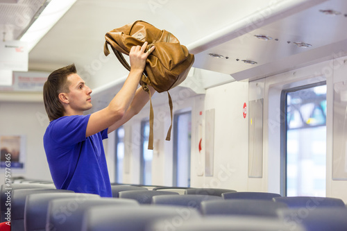 Young man putting luggage into overhead locker at train photo