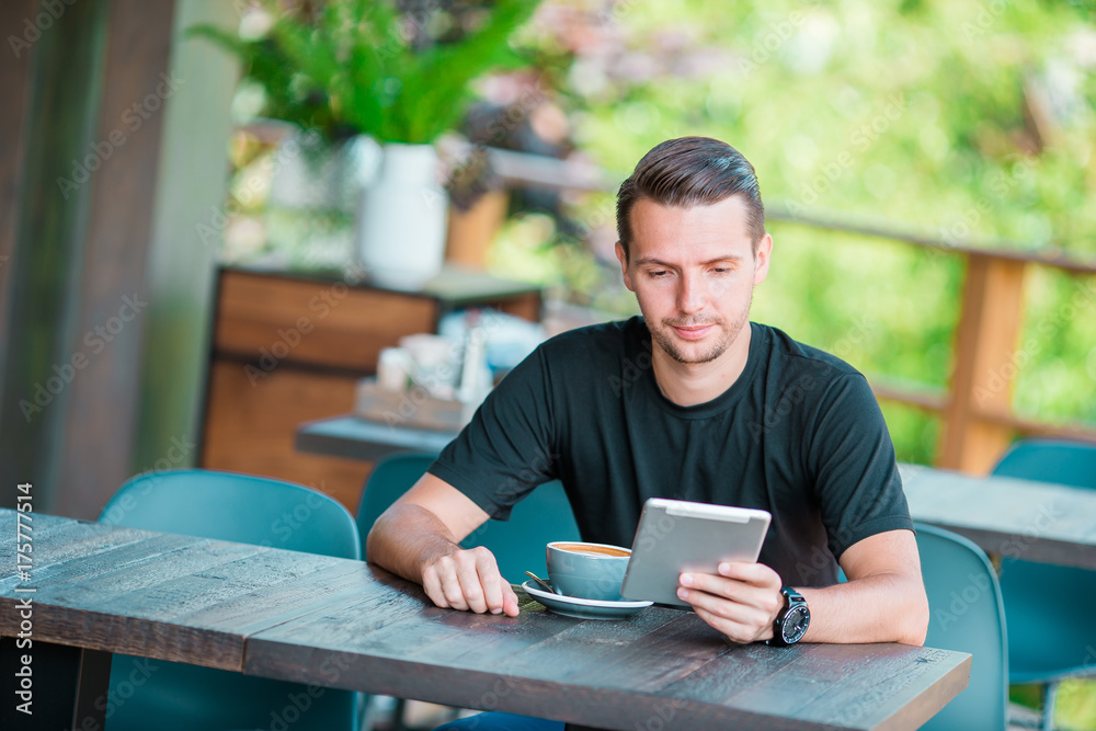 Young man with laptop in outdoor cafe drinking coffee. Man using mobile smartphone.