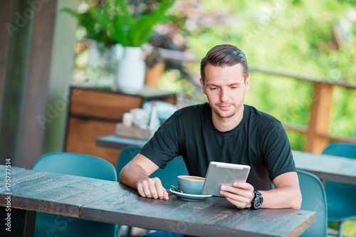 Young man with laptop in outdoor cafe drinking coffee. Man using mobile smartphone.