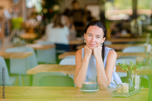 Beautiful woman having breakfast at outdoor cafe. Happy young urban woman drinking coffee