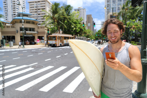 Photography Hawaii surfer man Honolulu city lifestyle using smart phone going to Waikiki beach surfing holding surfboard on street