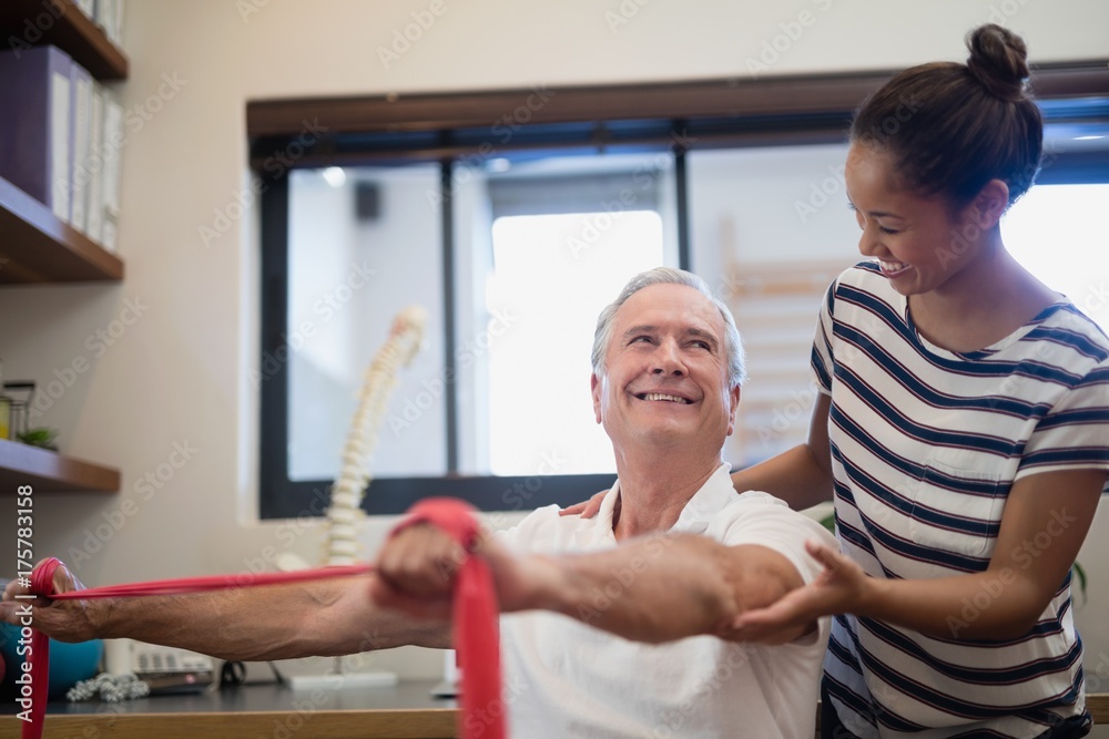 Obraz premium Smiling senior male patient pulling red resistance band while