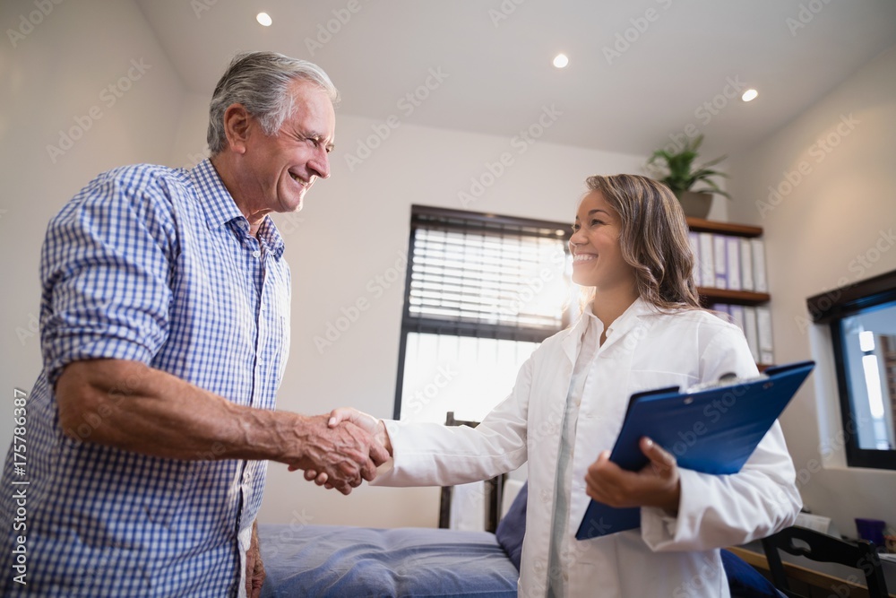 Obraz premium Smiling senior male patient and female therapist shaking hands