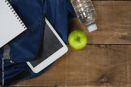 Schoolbag, apple, water bottle, book and digital table on wooden
