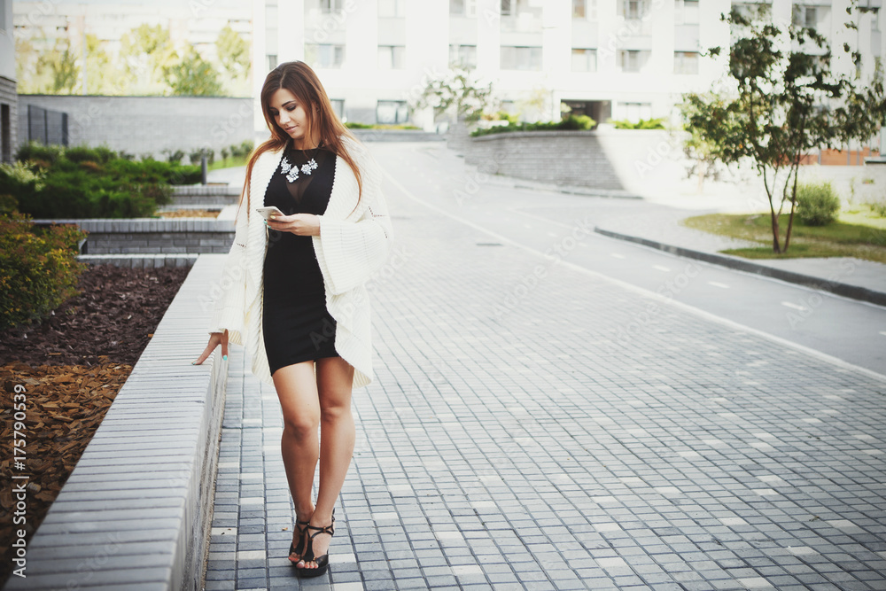 Beautiful young fashionable woman in a black short dress and white cardigan  posing in the city. Fashion photo Stock Photo | Adobe Stock