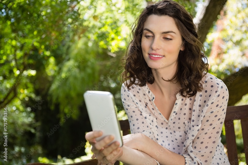 Woman sitting on bench and using digital tablet in garden on a Woman sitting on bench and using digital tablet in garden on a