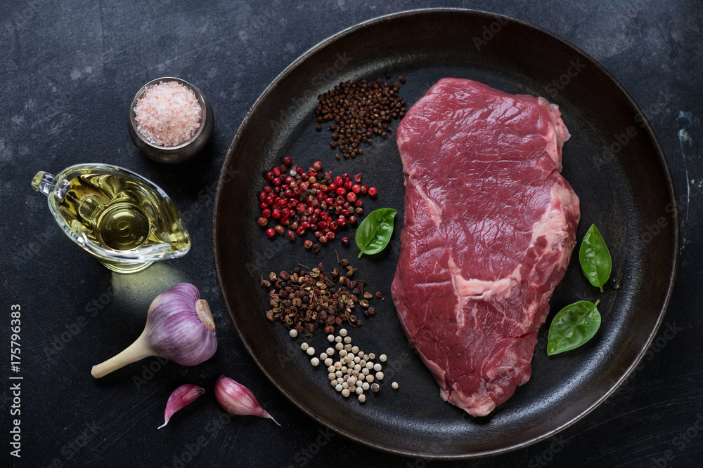 Above view of raw fresh ribeye beef steak with seasonings in a metal plate