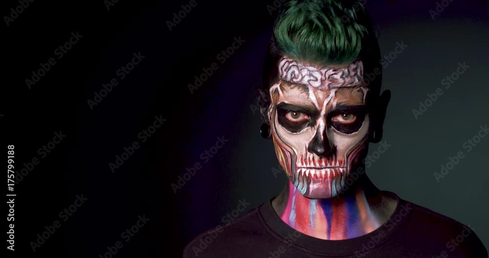 Man with colored skull makeup showing evil smile. Zombie man isolated on black background. Man with colored skull makeup showing evil smile. Zombie man isolated on black background.