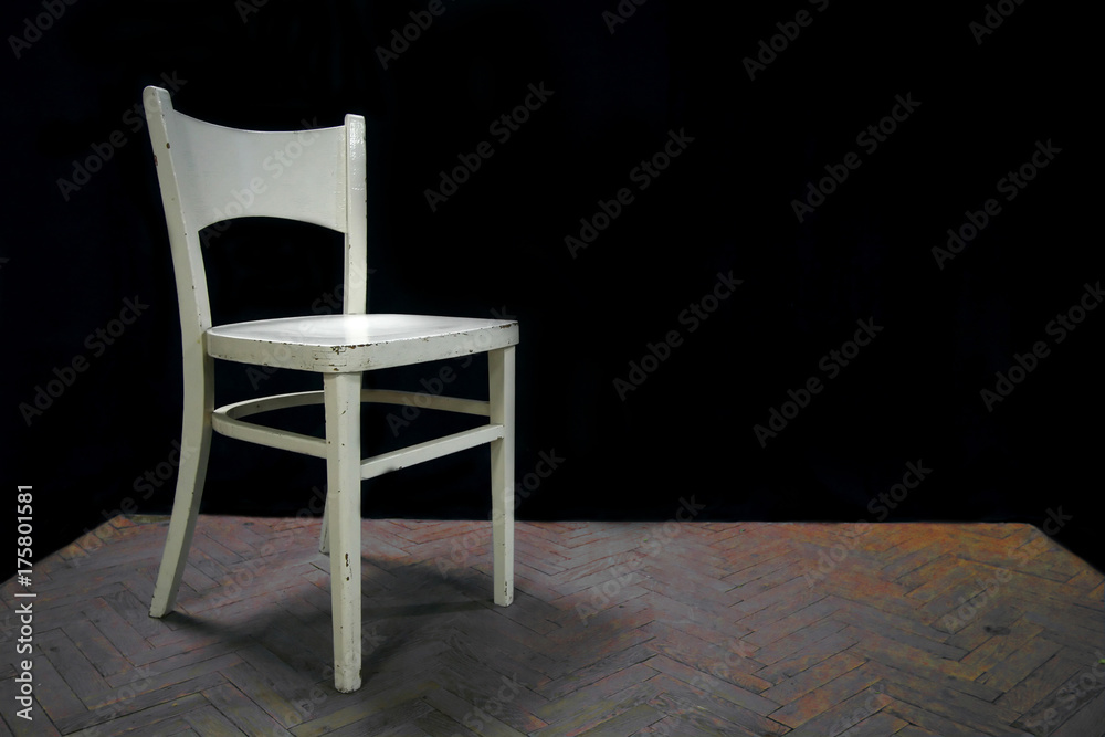 White, wooden chair standing alone on a wooden scene with a black background White, wooden chair standing alone on a wooden scene with a black background