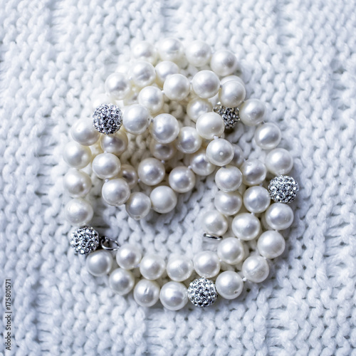 Pearl beads with strass inserts on a white lace knitted textile background are lined in a round curled circle shape.