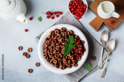 Healthy breakfast with chocolate corn rings, red currant berries, yogurt and tea on a gray concrete background. Selective focus. Top view. Copy space.