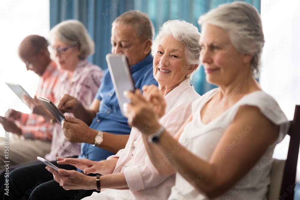 Fototapeta premium Senior people sitting on chairs while using digital tablets
