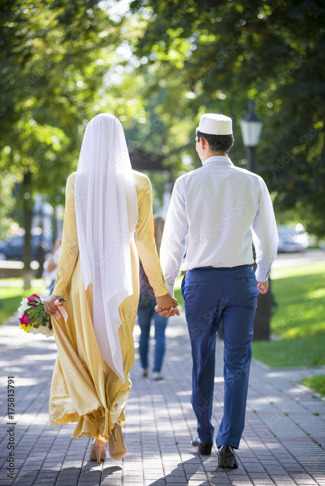 Muslim bride and groom hold hands and walk in the park on a bright, sunny day without faces. young couple nikah Muslim wedding. Islamic traditions. Muslim bride and groom hold hands and walk in the park on a bright, sunny day without faces. young couple nikah Muslim wedding. Islamic traditions.