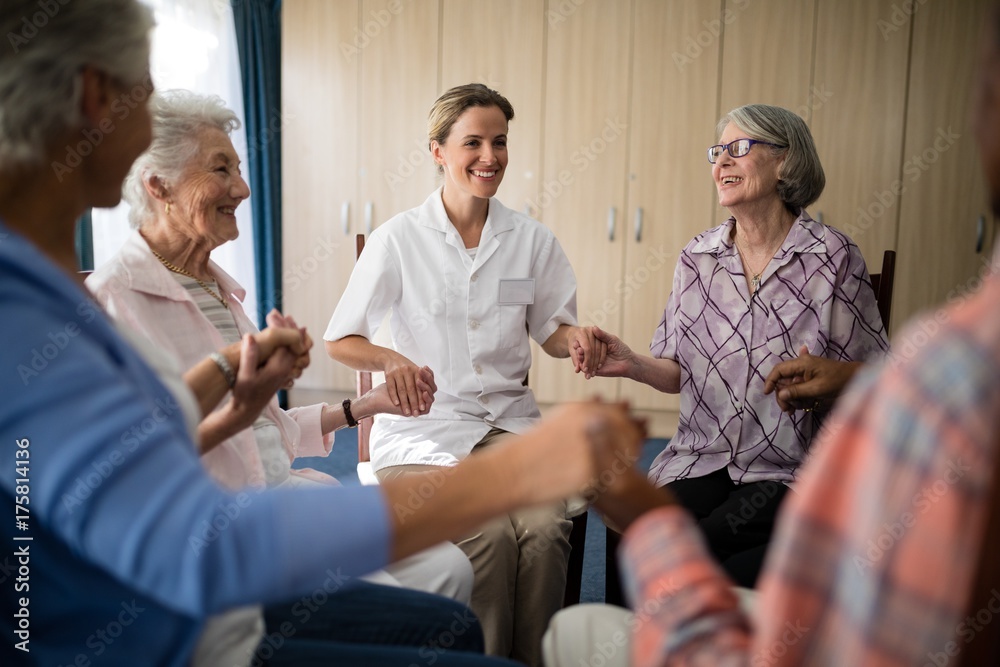 Smiling female doctor holding hands with seniors while sitting Smiling female doctor holding hands with seniors while sitting