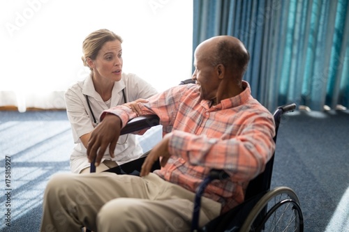 Female doctor kneeling while talking to disabled senior man on