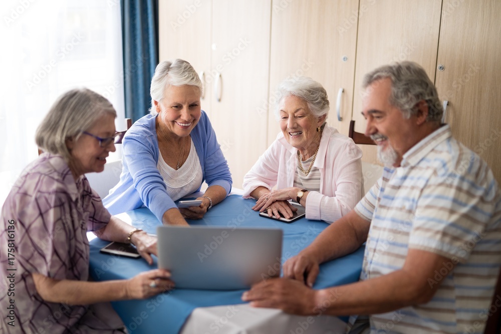Smiling senior man showing laptop to women at table Smiling senior man showing laptop to women at table