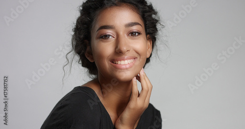 young girl with perfect light brown skin and beautiful curly black hair smiling at the camera in studio