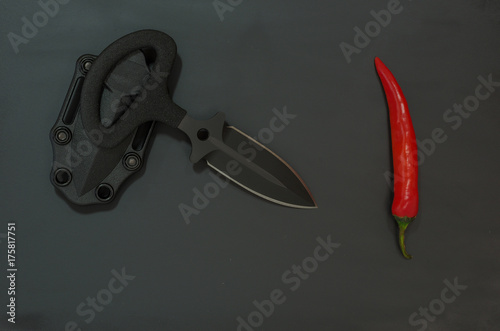 Sharp knife and chili pepper. Diagonal composition. Black and red. photo