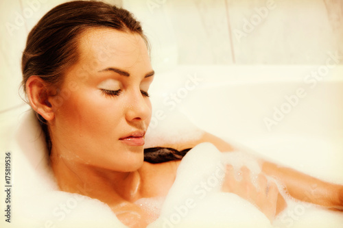 Young beautiful naked red-haired woman takes bubble bath