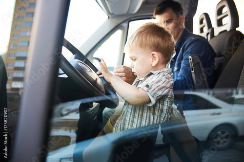 Portrait of cute little kid pressing the horn button on wheel sitting on front seat of car with dad