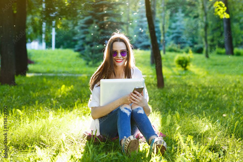 Young woman using cellphone and sitting on the grass on park at sunny day Young woman using cellphone and sitting on the grass on park at sunny day