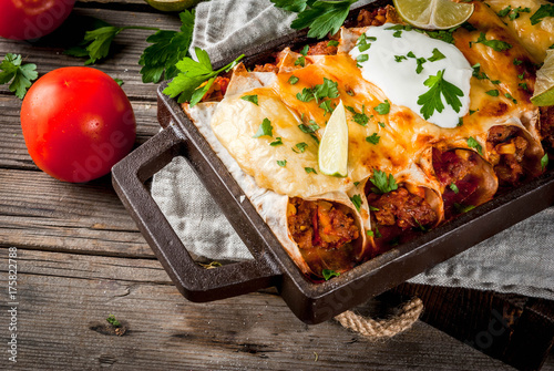 Mexican food. Cuisine of South America. Traditional dish of spicy beef enchiladas with corn, beans, tomato. On a baking tray, on old rustic wooden background. Copy space