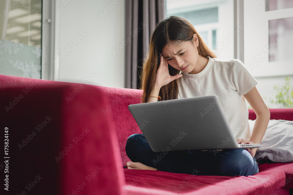 Naklejka premium Exhausted businesswoman having a headache while using laptop on red sofa, Business worry and Stress concept, Online shopping and marketing concept.
