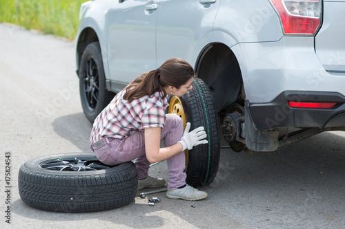 Young european woman changing car tire on rural road