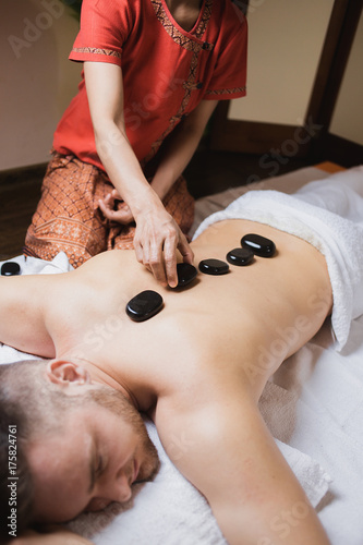man in wellness and spa setting having a hot stone therapy session photo