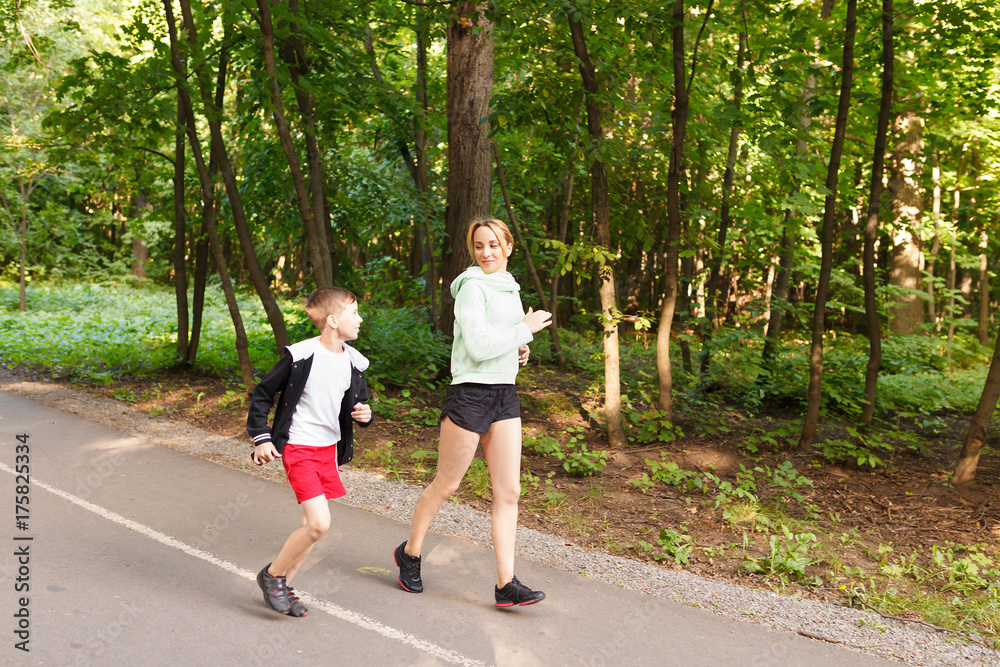 Young family jogging in the open air Happy mom with 9 years old child running at summer park Young family jogging in the open air Happy mom with 9 years old child running at summer park