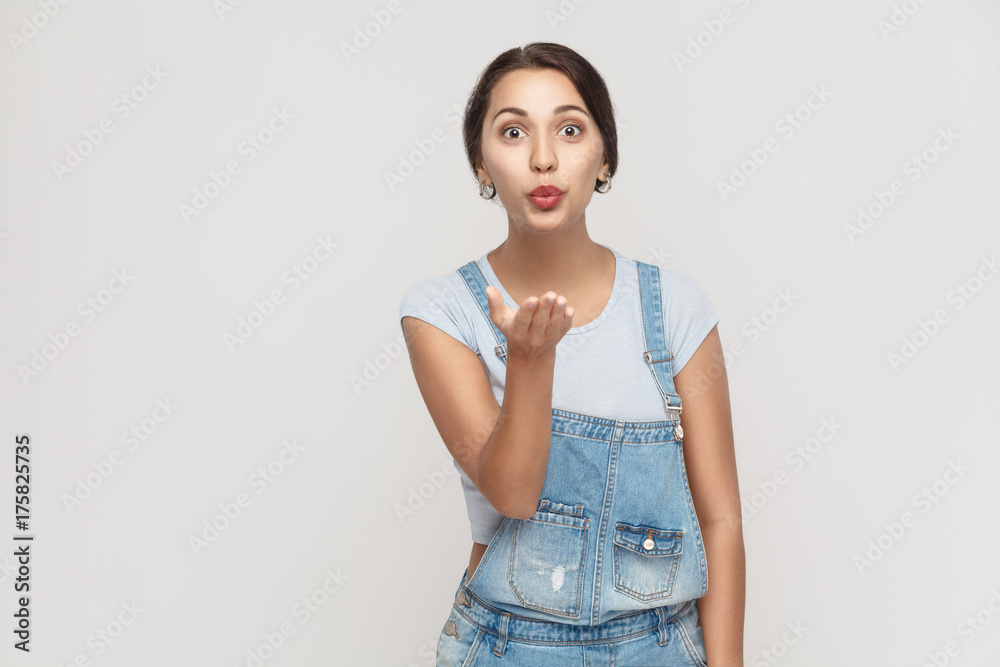 Fototapeta premium Young adult gypsy girl, posing over gray background , looking at camera and sending kisses.