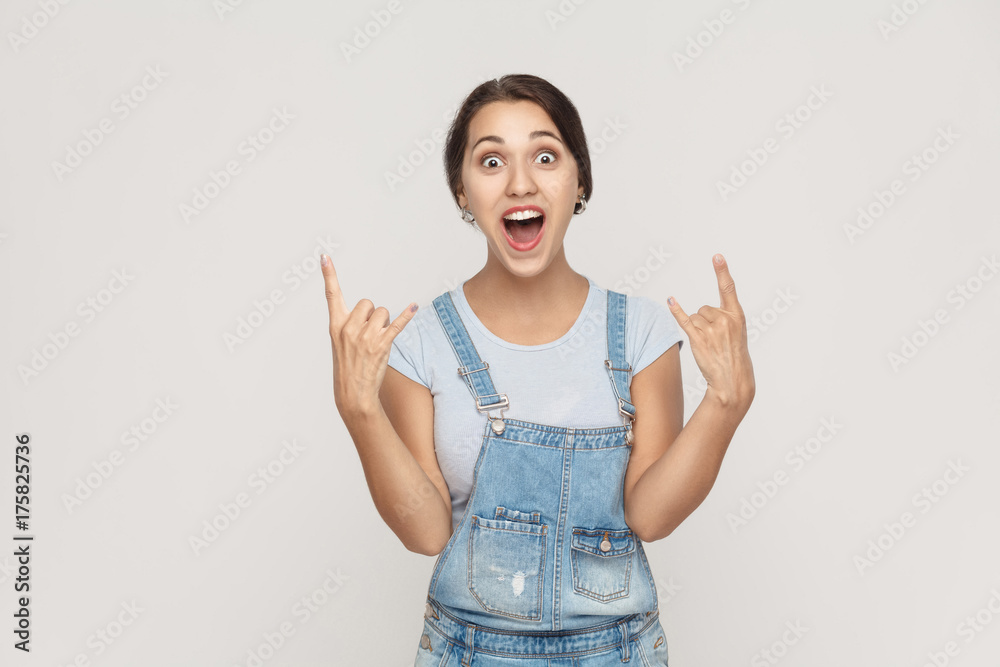 Rock n roll. Funny spanish woman in denim overalls, looking at camera with rock sing. Rock n roll. Funny spanish woman in denim overalls, looking at camera with rock sing.