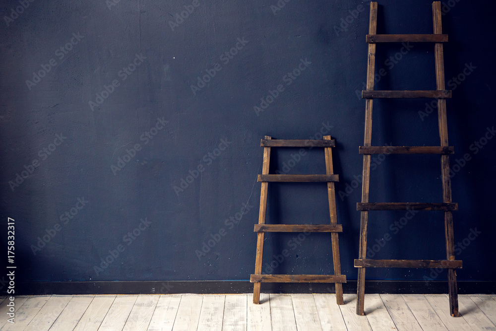 Fototapeta premium two wooden ladders stand at the blue wall on white floor